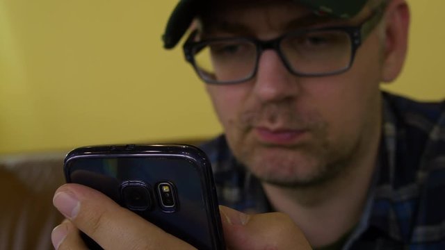 A Man In A Plaid Shirt Sitting On The Couch Using A Mobile Phone