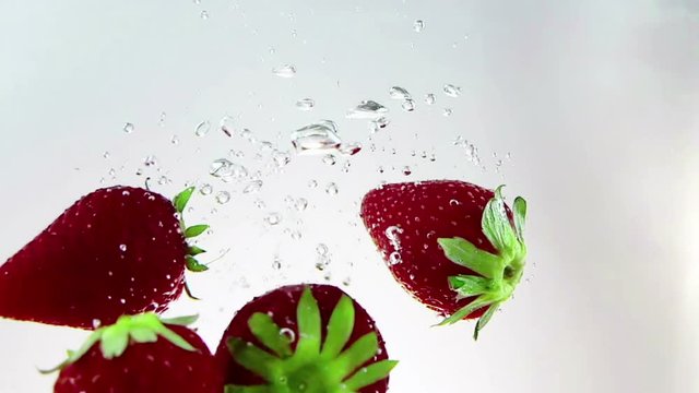 red fresh fruit strawberries falling into water with splash, shot in slow motion on white background, strawberry for health and diet, nutrition concept