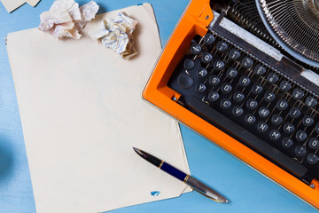 Workspace with orange vintage typewriter and empty paper on blue background