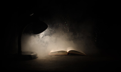 Open book near glowing table lamp on dark background, Lamp and opened book with smoke on background. Surreal