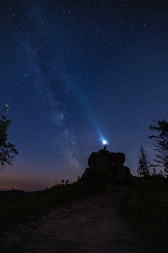 Tourist standing on the rock and pointing flashlight into night sky