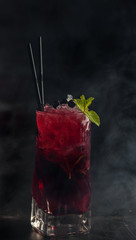 Berry (currant) lemonade with mint and ice in the smoke on a dark background.