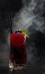 Berry (currant) lemonade with mint and ice in the smoke on a dark background.