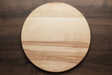 top view of wooden round board for pizza on brown table