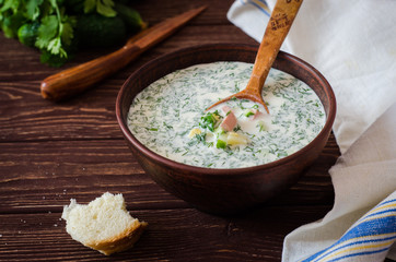 Okroshka. Summer light cold yogurt soup with cucumber, greens, eggs and dill on a wooden table. A traditional dish of Russian and Ukrainian  cuisine. Selective focus