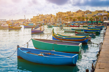 Fototapeta na wymiar Marsaxlokk, Malta - Traditional colorful maltese Luzzu fisherboats at the old village of Marsaxlokk with turquoise sea water and palm trees on a summer day