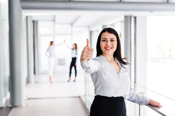 Beautiful modern business woman standing and showing thumbs up while behind are her work colleague