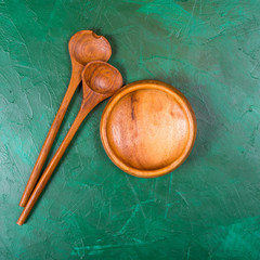 Wooden bowl for salad and wooden spoons on a green background