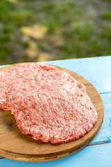 Raw minced meat burgers on the wooden round kitchen board
