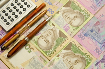 
A calculator, a pencil and two fountain pens lie on denominations of five hundred and two hundred hryvnia.