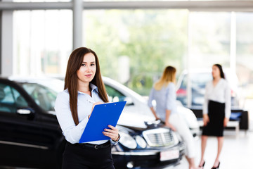 Bussines woman standing and writing on paper at modern car dealership