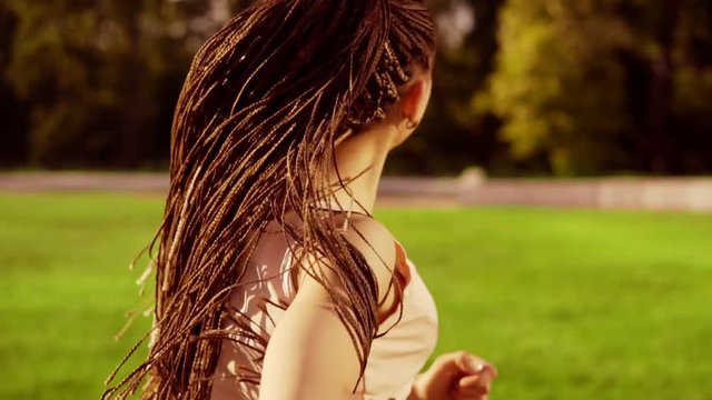 Long hair woman with dreads running in park and turning around looking in camera. Back of running woman in slow motion.