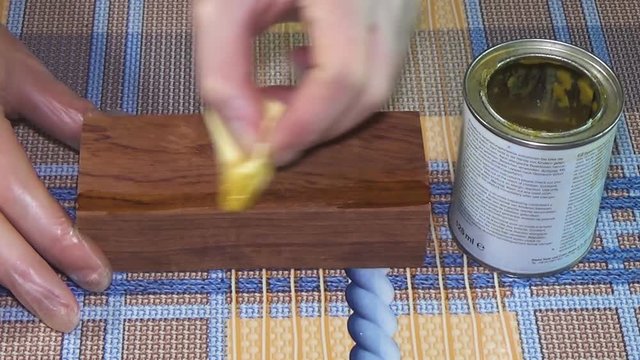 Wood beam palisander. The bar of solid wood is covered with stain. The girl covers a bar of rare wood with lacquer. The joinery impregnates the wood with wax.