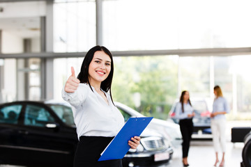Obraz premium Attractive business woman showing thumbs up while standing in modern car dealership