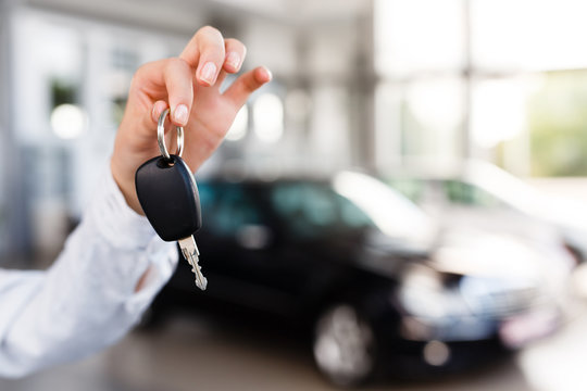 Attractive woman standing and holding car key in her hand at modern car dealership