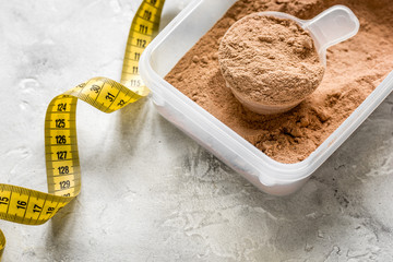 nutrition for workout with protein cocktail powder, measure tape on stone background close up