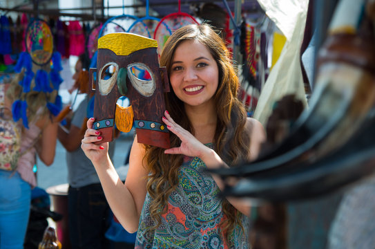 Close up of a young smiling beautiful woman holding in her hands a mask made of wood, in a store background