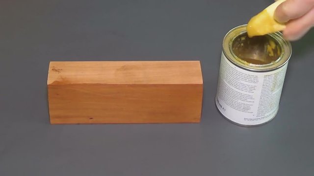 Pear wood. The bar of solid wood is covered with stain. The girl covers a bar of rare wood with lacquer. The joinery impregnates the wood with wax. Gray background. The end part of the wooden board.