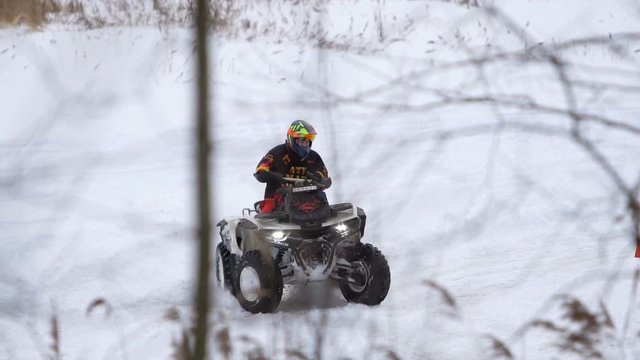 ATV race on the snow. Rider driving in the quadbike race. Man riding ATV in sand in protective clothing and a helmet. Racer rides a quad motorbike in the cross racing. Quadrocycle on the snow cover