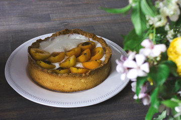 Homemade apricot pie in white plate on wooden table with rustic bouquet of flowers