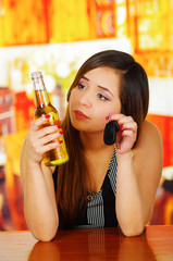 Portrait of a beautiful woman watching her beer and holding her car keys with her hand, in bar background