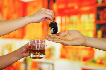 Close up of a hand holding a glass of whiskey and giving her keys to another person, in bar background