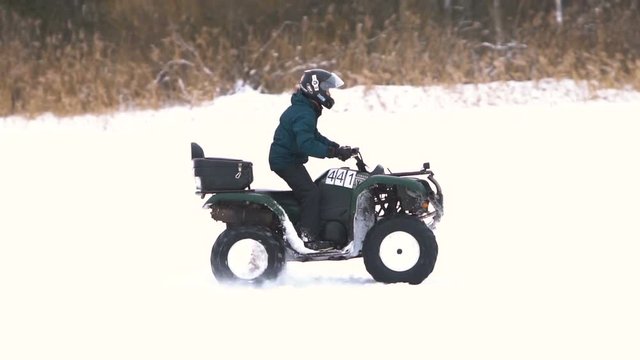 ATV race on the snow. Rider driving in the quadbike race. Man riding ATV in sand in protective clothing and a helmet. Racer rides a quad motorbike in the cross racing. Quadrocycle on the snow cover