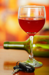 Close up of a cup of red wine with car keys on wooden tablea with a blurred green botle of wine behind