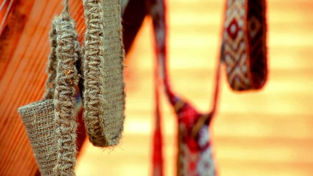 Wicker vintage bast shoes hanging on street. Traditional old bast shoes and ribbons with ethnic pattern in background. Close up national woven slavic basketry shoes. Slavic country wicker shoes