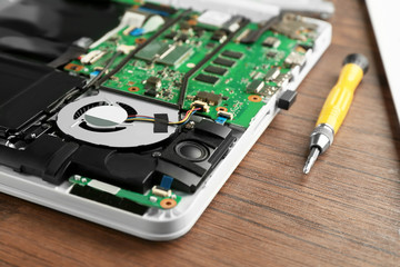 Dismantled laptop and screwdriver on wooden table. Concept of computer repair