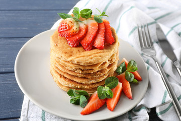 Delicious coconut pancakes with sliced strawberry and mint on wooden table