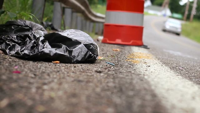 Garbage bag and dirty ugly litter on the side of a windy road 