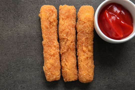 Delicious fried cheese sticks and bowl with sauce on grey background