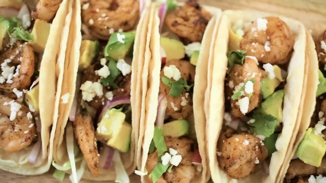 Close up of fresh chipotle shrimp tacos with cotija cheese on a white corn tortillas