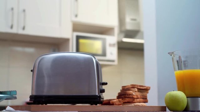TOASTER IN THE KITCHEN, ON THE TABLE. TURNED ON. HEALTHY BREAKFAST. JUICE, APPLE AND TOAST. DOLLY SHOT, CAMERA SLIDING FORWARD. BLUR TO SHARP