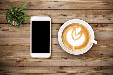 Top view of Cup of coffee with heart pattern in a white cup and smart phone on wooden background