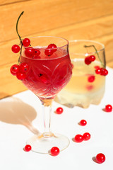 Pink and white champagne wine jelly with red currant in a glass, bright daylight, on white and wooden background. Front view