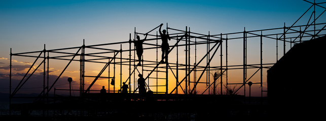 Construction workers working on scaffolding. - obrazy, fototapety, plakaty