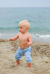 Blond baby standing on the beach on a cloudy day