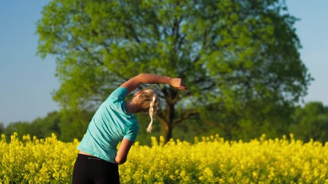 Fitness training of an gild at open air. Blooming fresh yellow rapeseed field with an big oak tree in background
