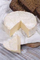 Brie type of cheese. Camembert cheese. Fresh Brie cheese and a slice on a wooden board with black bread slice. Italian, French cheese.