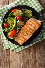 Salmon grilled with zucchini salad, arugula, pepper and tomatoes close-up on the table. vertical top view
