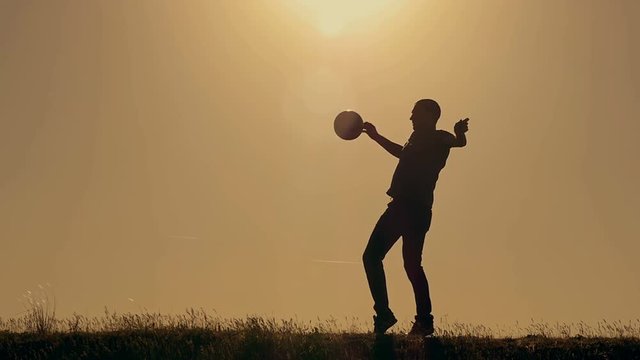 Football player practicing with the ball at sunset
