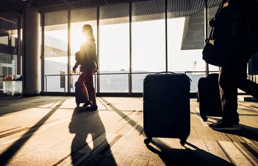 Fotobehang Luchthaven Silhouet van een vrouw die met bagage loopt bij het raam van de luchthaventerminal bij zonsopgang, reisconcept, reislevensstijl
