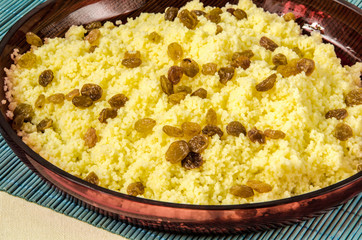 Plate with freshly cooked Moroccan couscous with raisins on blue straw background