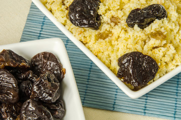 Plate with freshly cooked Moroccan couscous and with prunes on blue straw background