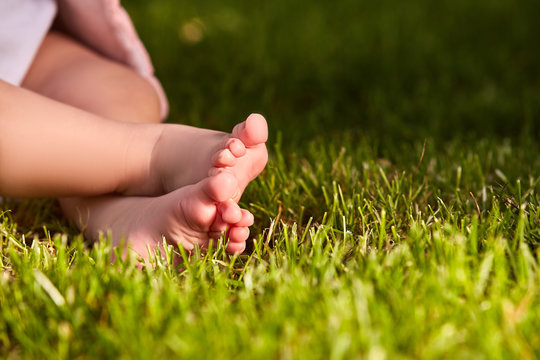 Close up of baby's feet on the green grass on the meadow at warm day.