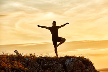 Silhouette of the man practicing yoga on the hill against beautiful sunset.