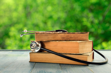 Stack of old books with stethoscope on wooden table