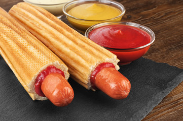 French hot dog and bowls with sauces on a slate board. Fast food.
